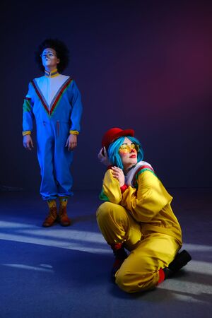 Two clowns a man and a woman with makeup in colored tracksuits in the style of the 80s or 90s posing against a trendy neon background.Party disco 80s 90s vibes.Creative art purple color styleの写真素材