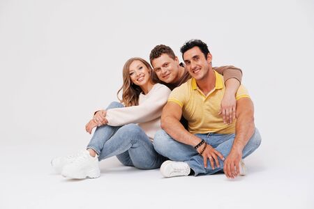 Three friends are sitting on the floor, hugging and smiling on a light background. Friendship...