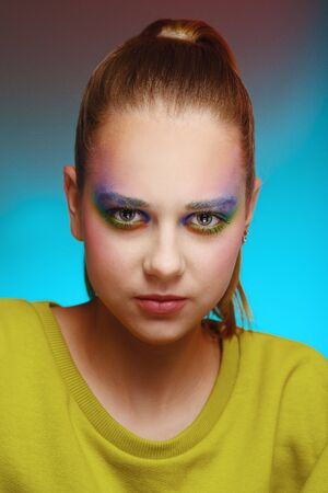Close-up portrait of a beautiful young girl in a green knitted dress with bright color makeup on a blue backgroundの写真素材