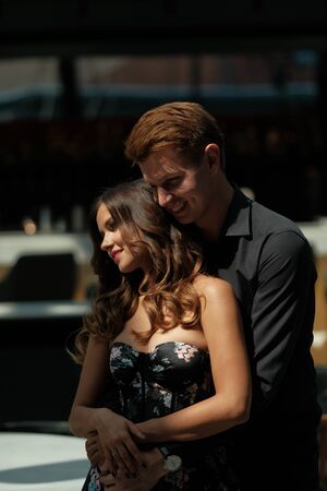 Young beautiful couple - a girl in a magnificent dress and a guy in a black shirt and trousers are in a building with a beautiful interior and high glass ceilings. Concept of romance and loveの写真素材