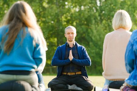 A group of young people meditate outdoors in a park. Meditation and yoga, healthy lifestyle concept. Spiritual Restoration. Wellbeing, wellness conceptの写真素材
