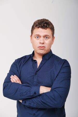 Studio portrait of man with hand on head against plain background. A man aged 30-35 years in a blue shirt shows different human emotionsの写真素材