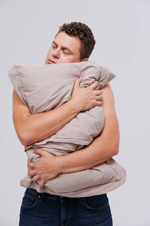 Studio portrait of sleepy man hugging pillow against plain background. The concept of a healthy sleep and a healthy lifestyleの写真素材