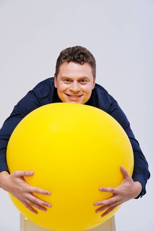 Studio portrait of man posing with big yellow ball against plain backgroundの写真素材