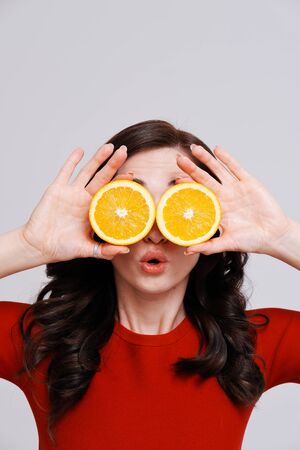 Studio portrait of young brunette with oranges covering eyes on plain backgroundの写真素材