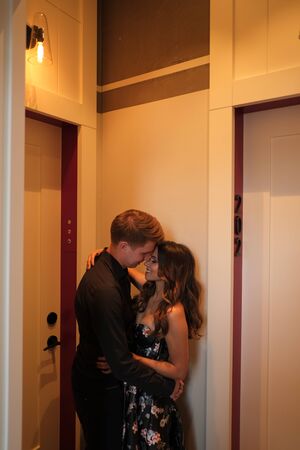 A young couple - a girl in a magnificent dress and a guy in a black shirt and trousers hug and kiss in a hotel room. Concept of romance and loveの写真素材