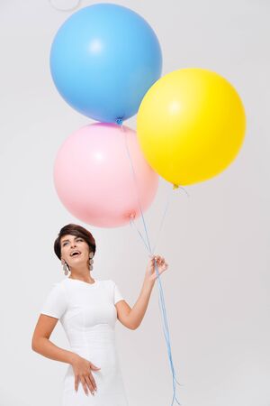 Studio portrait laughing woman age 35-40 years with bunch of colorful balloons against plain backgroundの写真素材