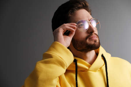 Fashionable young man 25-30 years old in sunglasses and a yellow sweatshirt posing against the background of a gray wall.の写真素材