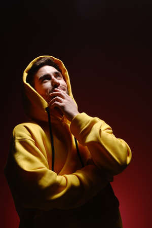 A young man of 25-30 years old in a yellow sweatshirt is standing against a red wall. The concept of...