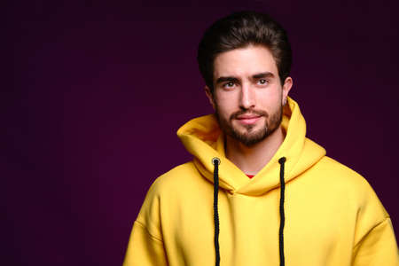 A young man of 25-30 years in yellow sweatshirt emotionally poses on a purple background. The concept of modern fashion photography. Brutal man portraitの写真素材
