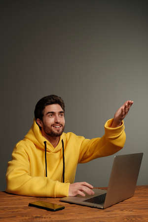 A young guy with different emotions in a yellow sweatshirt works using a laptop and smartphone. Remote work, coworking, freelanceの写真素材