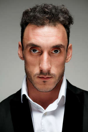 Close up portrait of a man 30-34 years old in a white shirt and a black jacket on a gray background. A man with curly hair, big eyes and bristles shows different human emotions.の写真素材