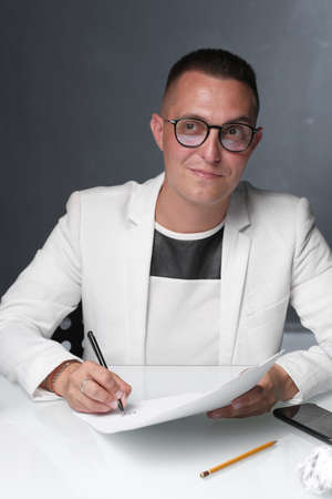 Businessman 30-35 years old in a white jacket signs important documents while sitting at the table. Closeup male portrait. Business and deal concept.の写真素材