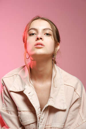 Portrait of a young beautiful girl 20-25 years old with green eyes and long hair. A girl in a pink denim shows different emotions and poses on a pink background.の写真素材