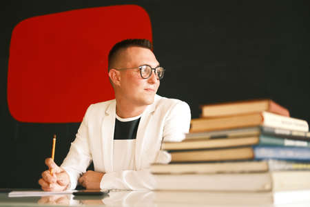 A young school teacher a man in a white jacket and glasses checks the homework of his students and prepare for a new lesson. Education, school, college and university concept.の写真素材