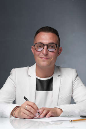 Businessman 30-35 years old in a white jacket signs important documents while sitting at the table. Closeup male portrait. Business and deal concept.の写真素材