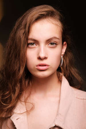 Close-up portrait of a young beautiful girl 20-25 years old with green eyes and long hair. Girl in a pink jacket poses on a dark background. Fashion photography conceptの写真素材