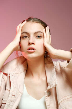 Portrait of a young beautiful girl 20-25 years old with green eyes and long hair. A girl in a pink denim shows different emotions and poses on a pink background.の写真素材