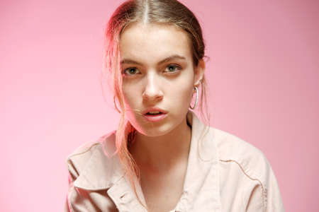 Portrait of a young beautiful girl 20-25 years old with green eyes and long hair. A girl in a pink denim shows different emotions and poses on a pink background.の写真素材