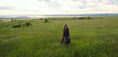 A young woman of 25-30 years old with curly red hair, in a green dress and in a diadem with feathers...