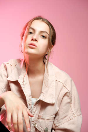 Portrait of a young beautiful girl 20-25 years old with green eyes and long hair. A girl in a pink denim shows different emotions and poses on a pink background.の写真素材