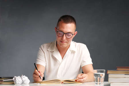 A young student guy sits at a table and is engaged in scientific work and study. Student's desk - books, textbooks, stationery. School and education concept. First school dayの写真素材