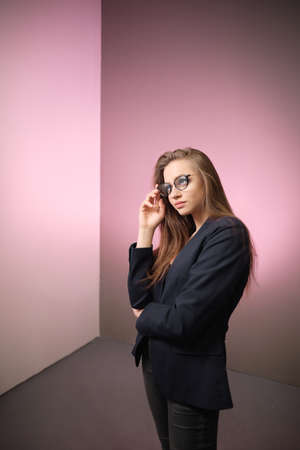 A young girl 20-25 years old in glasses and a trouser suit in the image of a teacher posing against a bright background.の写真素材