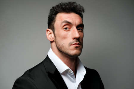 Close up portrait of a man 30-34 years old in a white shirt and a black jacket on a gray background. A man with curly hair, big eyes and bristles shows different human emotions.