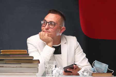 A young school teacher a man in a white jacket and glasses checks the homework of his students and prepare for a new lesson. Education, school, college and university concept.の写真素材