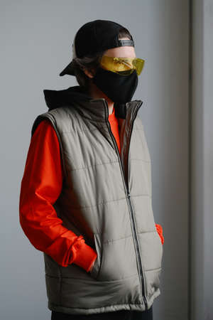 A young man of 25-30 years old in a black protective mask, yellow goggles, a cap and a red jacket posing on a gray background. Coronavirus protection.の写真素材