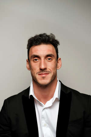 Close up portrait of a man 30-34 years old in a white shirt and a black jacket on a gray background. A man with curly hair, big eyes and bristles shows different human emotions.の写真素材