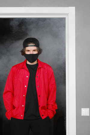 Portrait of a young man of 25-30 years old in a black protective mask, cap and red jacket. A man...
