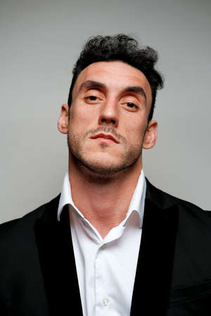 Close up portrait of a man 30-34 years old in a white shirt and a black jacket on a gray background. A man with curly hair, big eyes and bristles shows different human emotions.の写真素材
