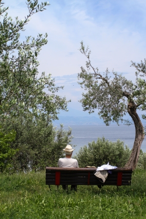 lonely senior man sitting on a bench next to lake Garda, italy  man s face cannot be seenの写真素材