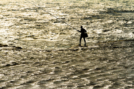 fisherman with a rod stand alone in the seaの写真素材