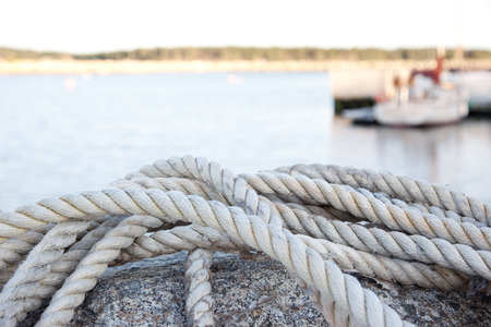 A close up of a dock rope, water surface and coast in the background.の写真素材