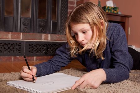Young blond girl lying on the floor drawing.の写真素材