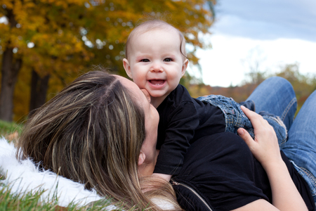 Cute little happy baby girl with her mother lying on the grass, playing and smiling.の写真素材