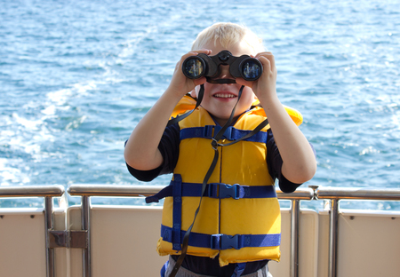 a cute boy holds binoculars and looks at his subject, ocean behindの写真素材