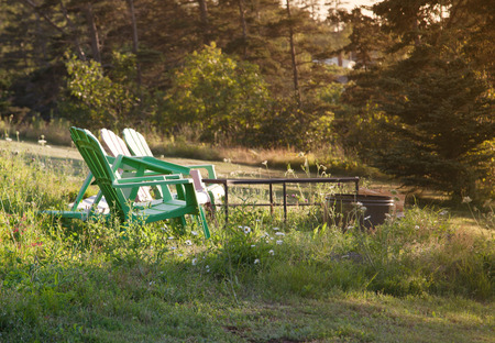 in the summer sun, three green lawn chairs sit empty around a black fire pitの写真素材