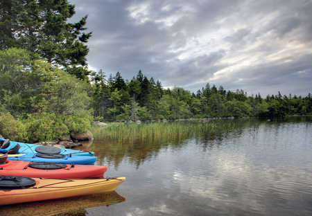 a group of four, brightly coloured kayaks wait on the lake or shore in the early morningの写真素材