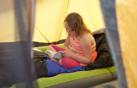 little girl reading inside her tent, framed by tentの写真素材