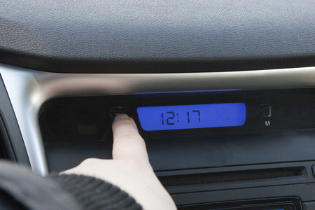 a hand pushes the hour button on a car clock to change the time