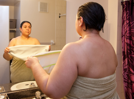 Woman stands in front of reflection as part of morning shower routine, ready to towel dry hairの写真素材