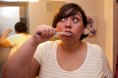 A woman brushes her teeth in the bathroom and raises her eyes in thoughtの写真素材