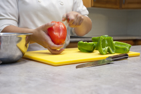 Close up of hands slicing a red bell pepper on a cutting board in the kitchenの写真素材