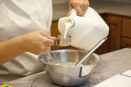 Person mixing and measuring milk into a cup in the kitchenの写真素材