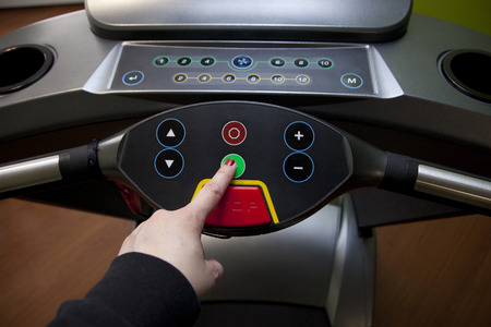Get ready to run- hand pushes the green start button on a treadmill in a home gym