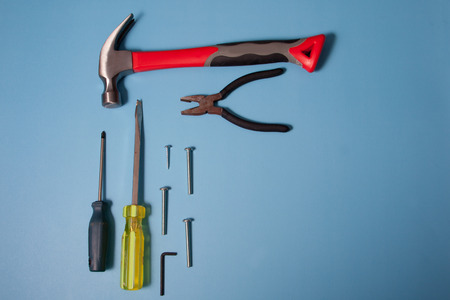 Lay flat view of some tools including a hammer, pliers and screwdriver on a blue background