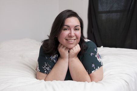 A relaxed happy woman lays on her bed at home looking at the camera in a portrait